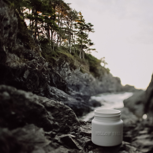 White ceramic candle jar with embossed label on rocky ground.