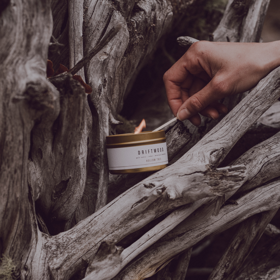 Travel candle in white-and-gold tin, lit wick, DRIFTWOOD label on front