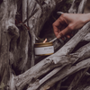 Travel candle in white-and-gold tin, lit wick, DRIFTWOOD label on front