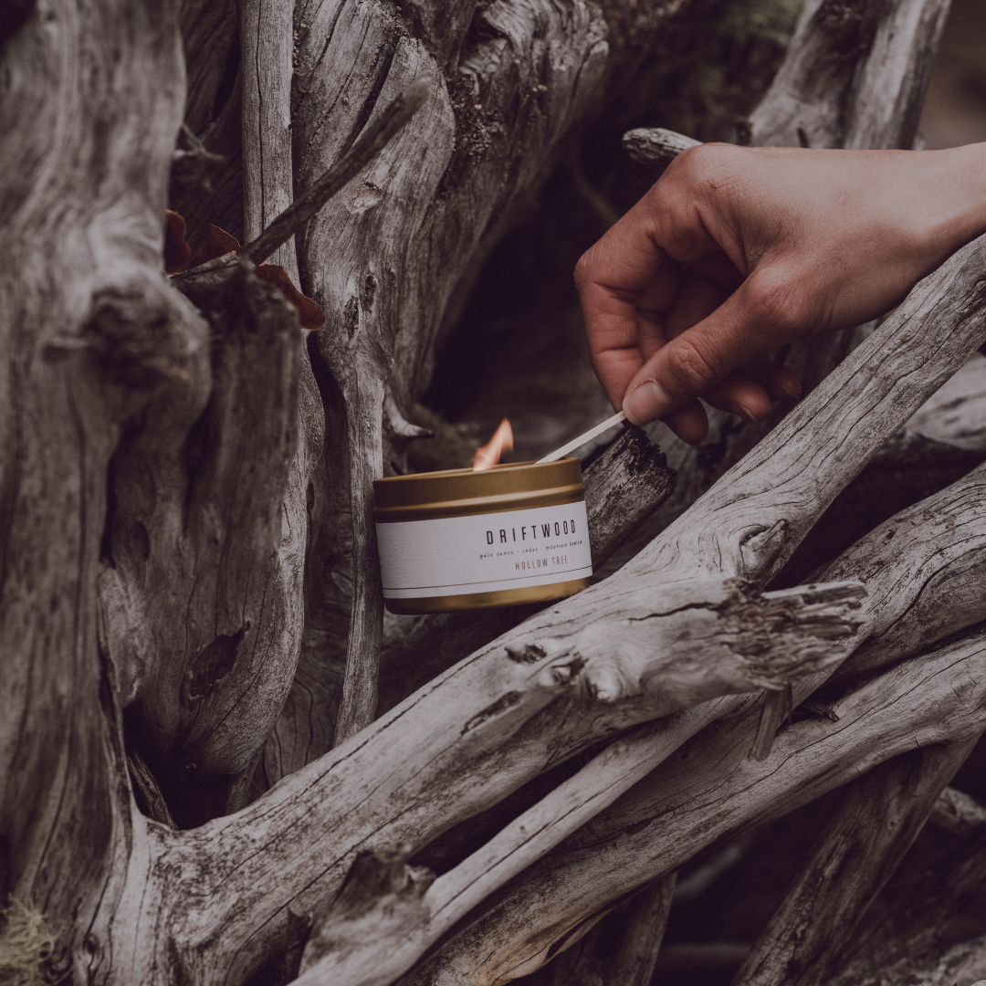Travel candle in white-and-gold tin, lit wick, DRIFTWOOD label on front