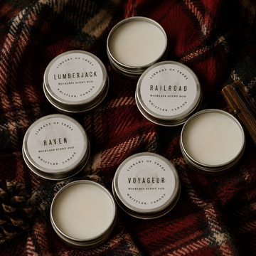 Five round metal scent pod tins with labels: Lumberjack, Railroad, Raven, Voyaguer