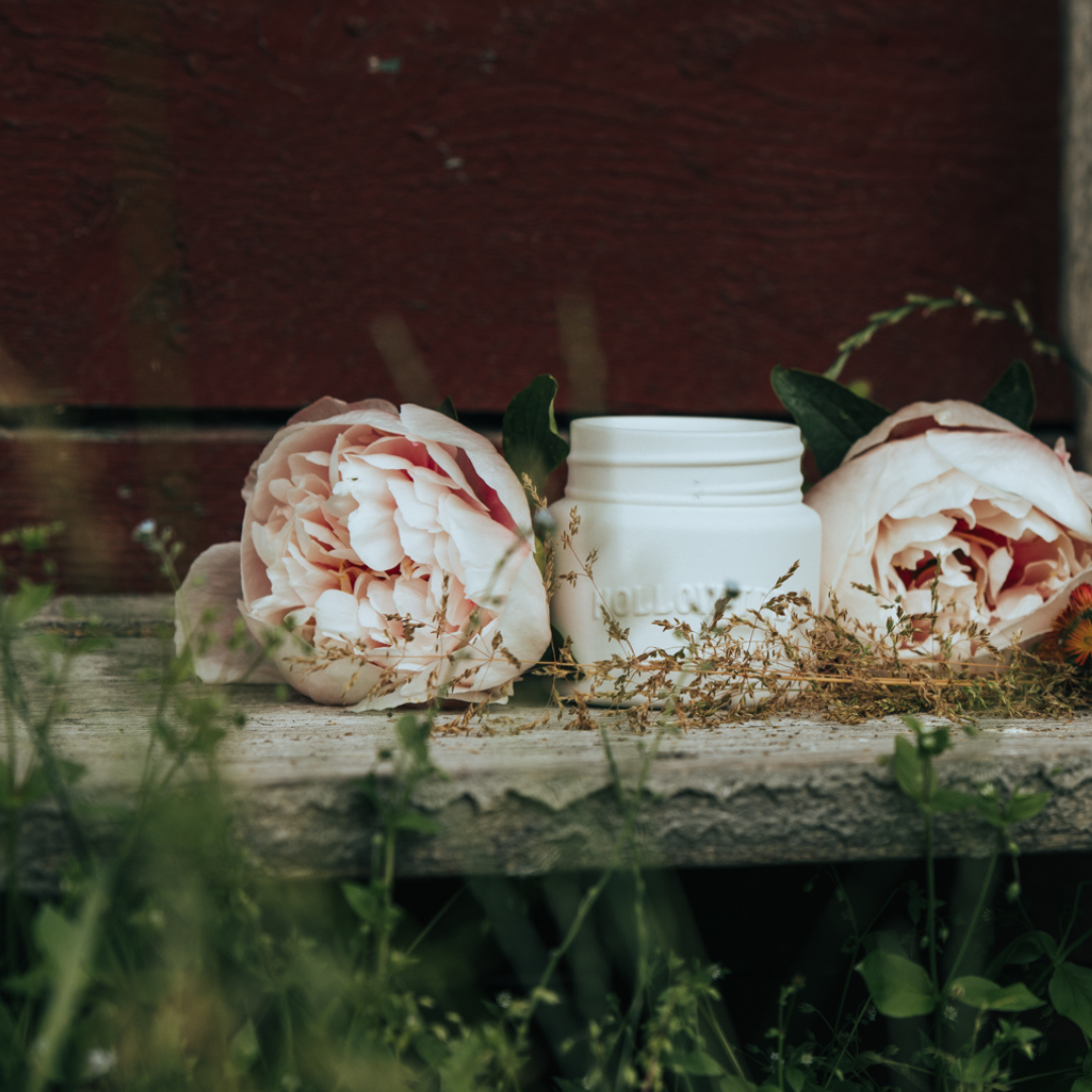 Ceramic candle in a white jar with two white flowers and greenery around it