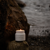 Scented candle in white glass jar with open lid, warm flame