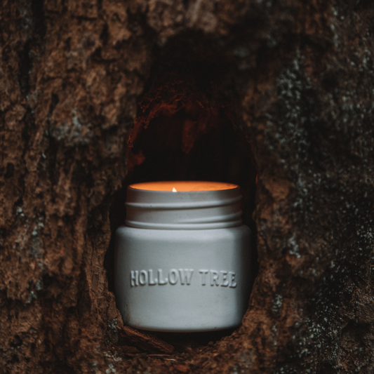Gray-blue jar candle close-up with “HOLLOW TREE” label and flame