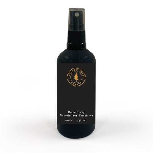 A black room spray bottle with a white label and gold accents, including the product name 'Voyageur Room Spray' and the scent notes 'Tobacco, Apple, Black Pepper'.