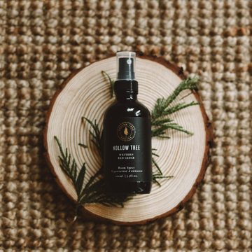 Room spray bottle with dark glass body and Hollow Tree label, on wood slice.