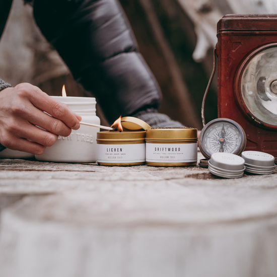 Travel candles in white-and-gold tins, lit wicks; Driftwood tin among them