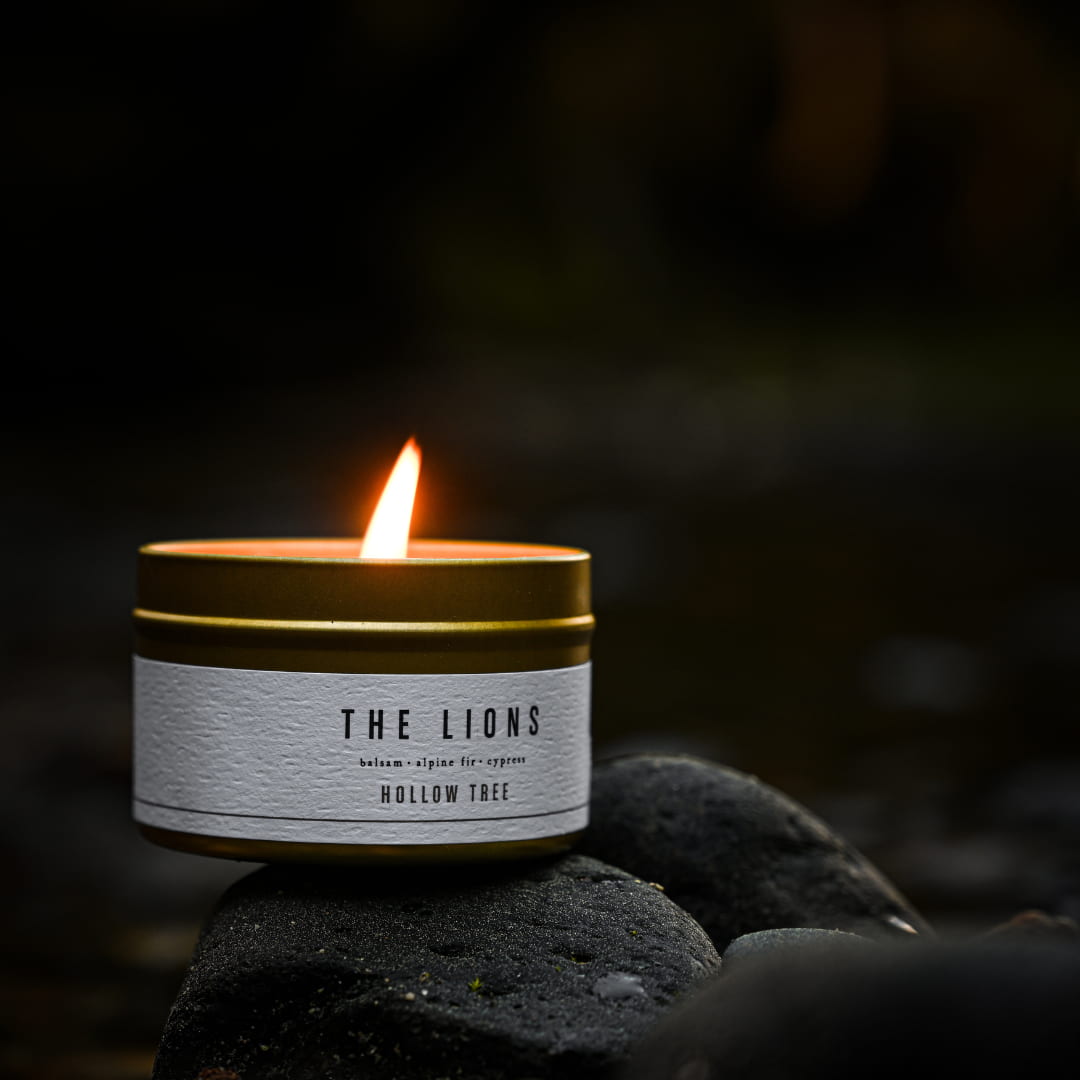 Scent candle in metal-lid jar, label reads The Lions and Hollow Tree