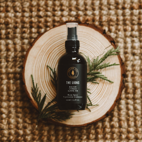 The Lions room spray bottle with black label and spray nozzle, on wooden slice