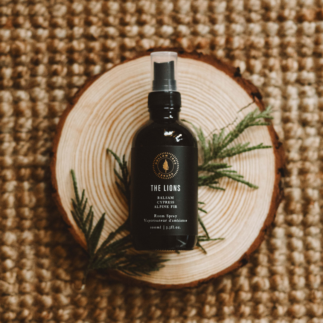 The Lions room spray bottle with black label and spray nozzle, on wooden slice