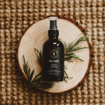 The Lions room spray bottle with black label and spray nozzle, on wooden slice