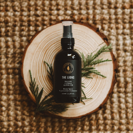 The Lions room spray bottle with black label and spray nozzle, on wooden slice