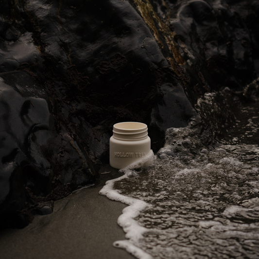 Ceramic candle jar with lit flame on dark rocky path