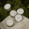 Set of tree-scent tin jars with round labels, on light gray cloth.